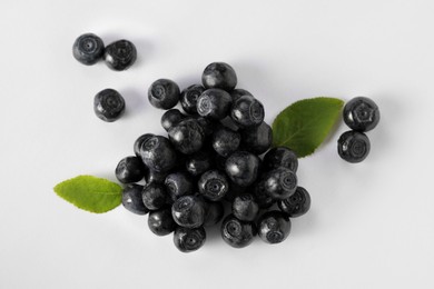 Photo of Pile of ripe bilberries and leaves on white background, flat lay