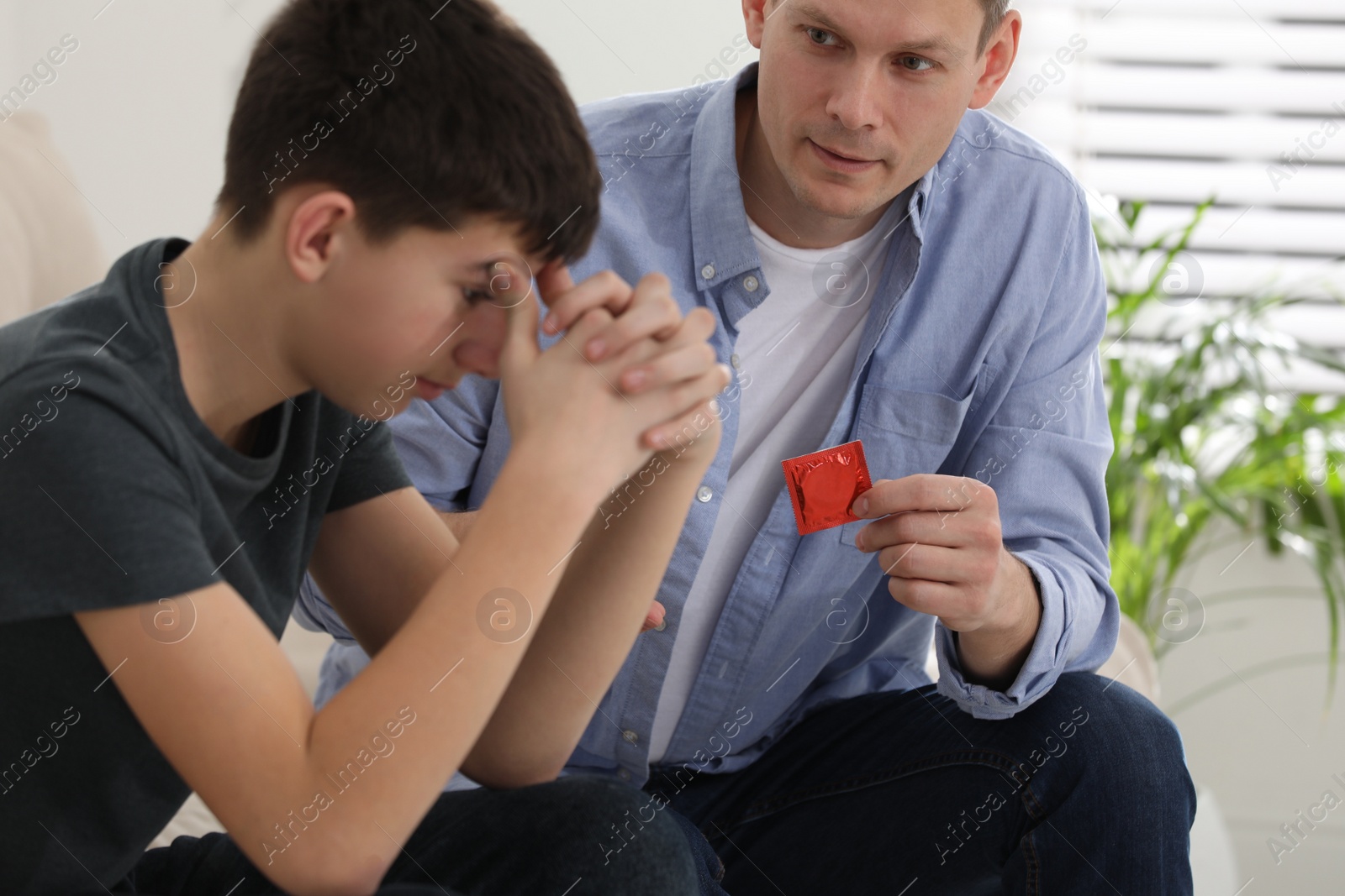 Photo of Father talking with his teenage son about contraception at home. Sex education concept