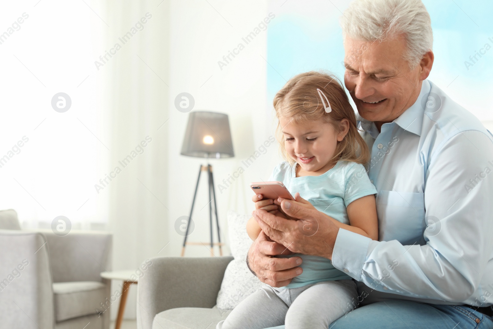 Photo of Little girl with her grandfather using smartphone at home, space for text. Family time