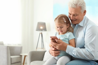 Photo of Little girl with her grandfather using smartphone at home, space for text. Family time