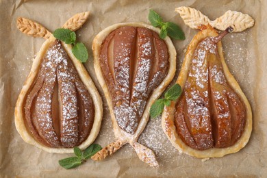 Photo of Delicious pears baked in puff pastry with powdered sugar and mint on parchment paper, top view