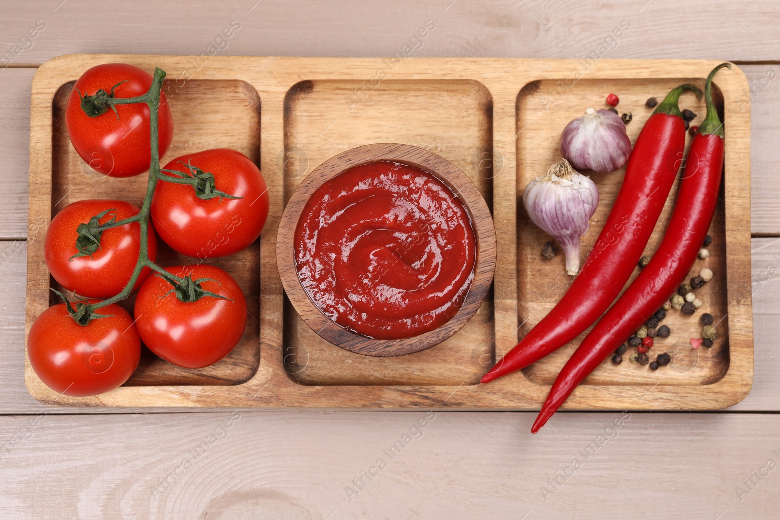 Photo of Plate with delicious ketchup in bowl, peppercorns and products on light wooden table, top view. Tomato sauce