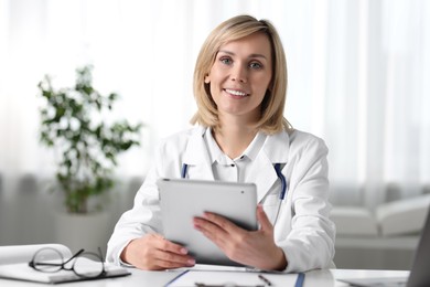 Photo of Smiling doctor with tablet having online consultation at table in office