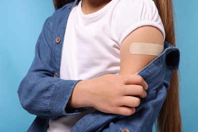 Photo of Girl with sticking plaster on arm after vaccination against light blue background, closeup
