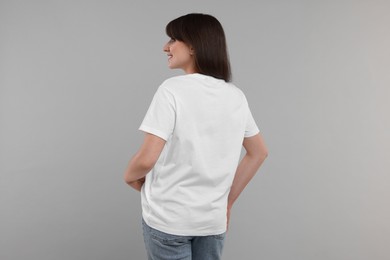 Photo of Smiling woman in white t-shirt on grey background, back view