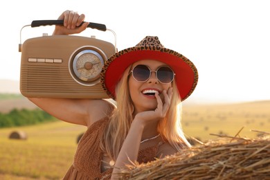 Happy hippie woman with receiver near hay bale in field