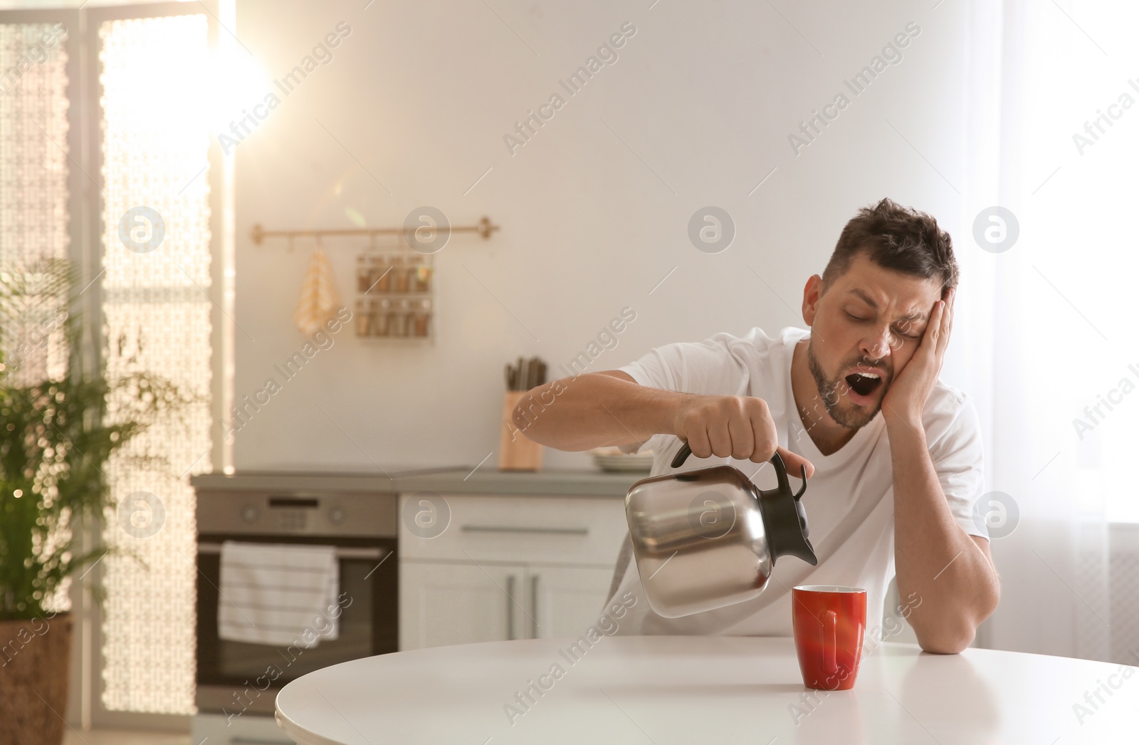 Photo of Sleepy man pouring coffee into cup at home in morning