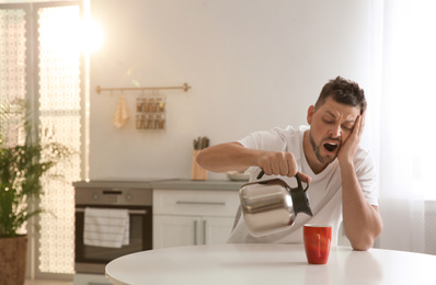 Sleepy man pouring coffee into cup at home in morning