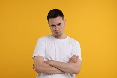 Resentful man with crossed arms on orange background