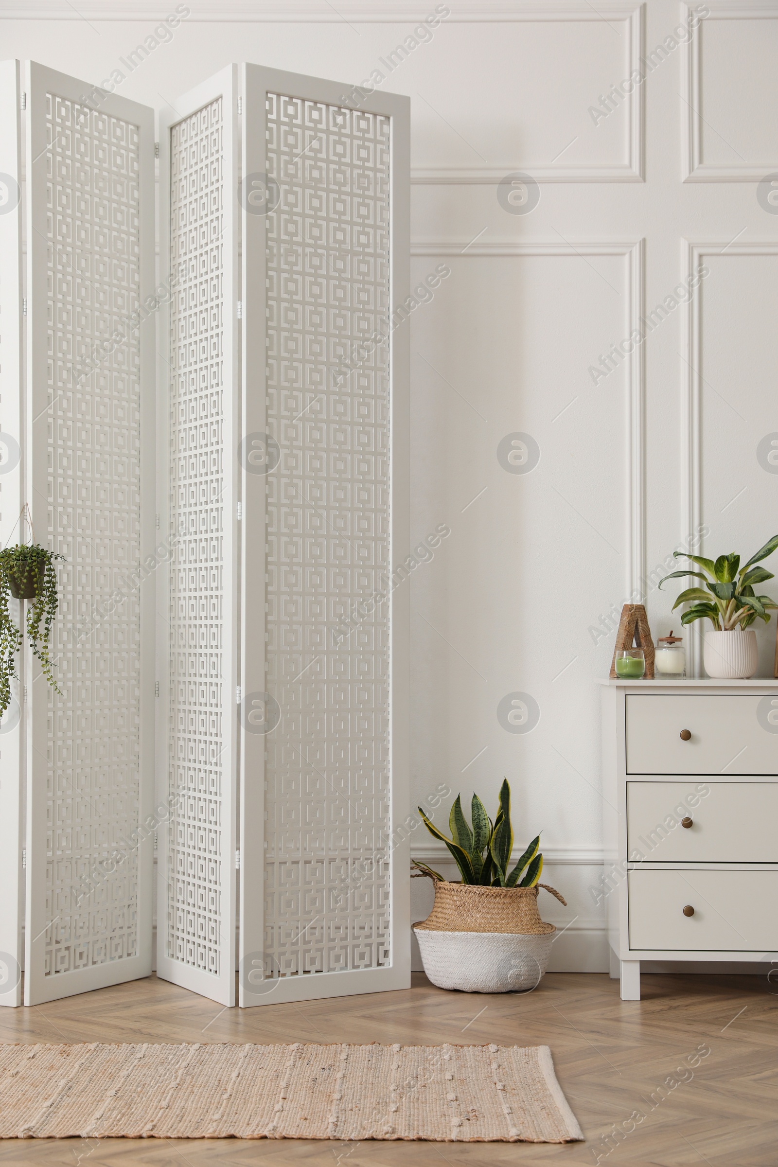 Photo of Stylish room with wooden folding screen and chest of drawers near white wall. Interior design