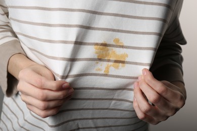 Woman showing shirt with yellow stain on grey background, closeup