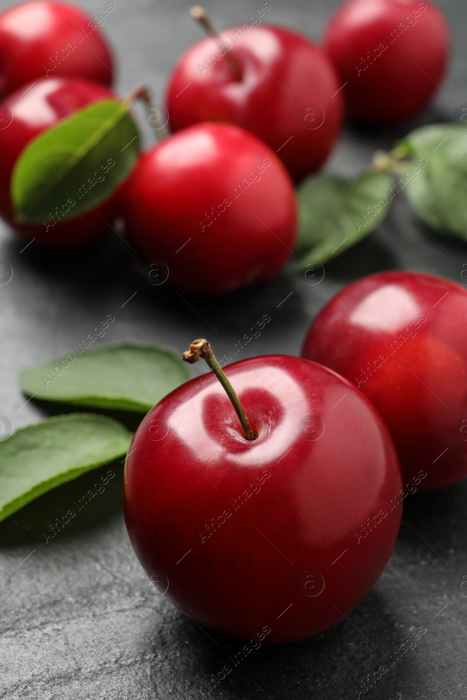 Photo of Delicious ripe cherry plums with leaves on black table, closeup