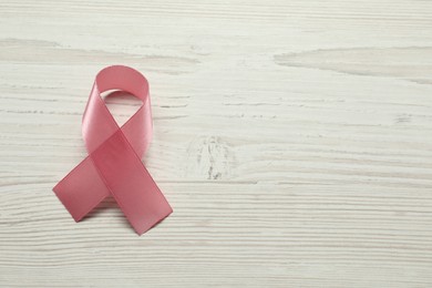 Breast cancer awareness. Pink ribbon on white wooden table, top view. Space for text