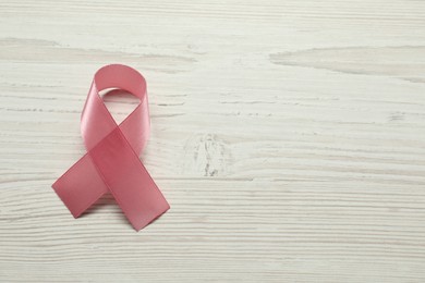 Photo of Breast cancer awareness. Pink ribbon on white wooden table, top view. Space for text