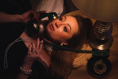Photo of Young woman with cigarette and vintage telephone crying under dim lamp light indoors in evening