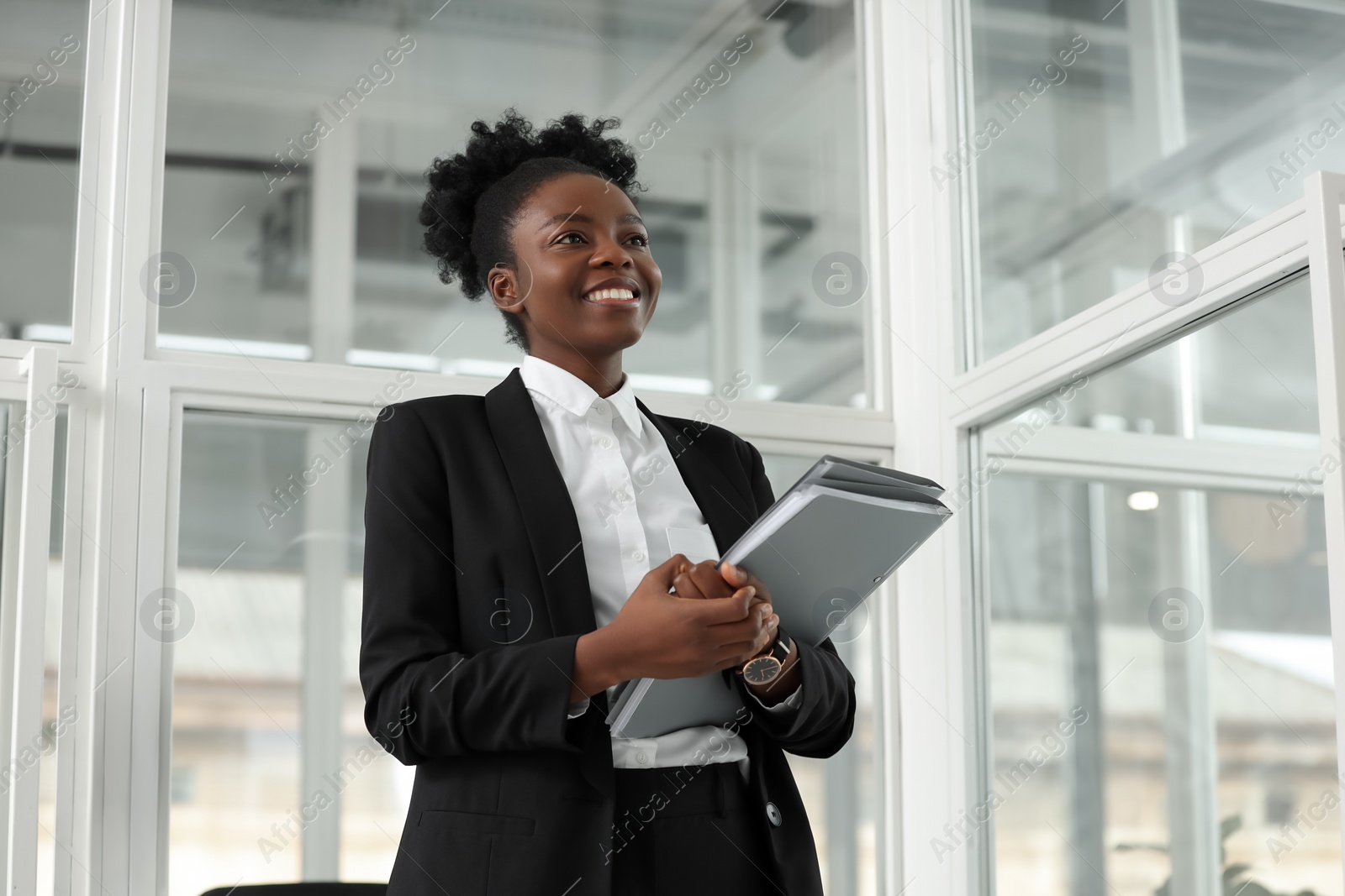 Photo of Happy woman with folders in office, low angle view. Lawyer, businesswoman, accountant or manager