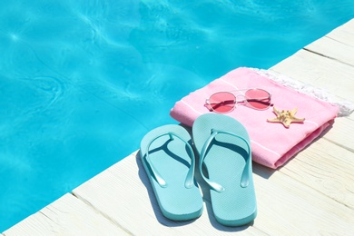 Beach accessories on wooden deck near swimming pool. Space for text