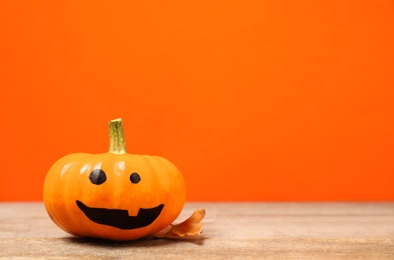 Photo of Pumpkin with scary face and fallen leaf on orange background, space for text. Halloween decor