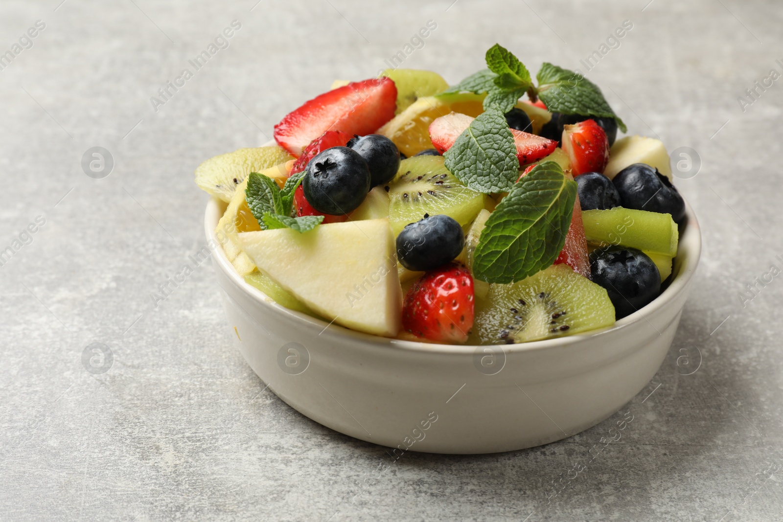 Photo of Tasty fruit salad in bowl on gray textured table, closeup. Space for text