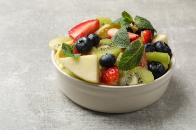 Tasty fruit salad in bowl on gray textured table, closeup. Space for text