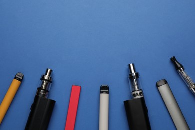 Photo of Many electronic smoking devices on blue background, flat lay. Space for text