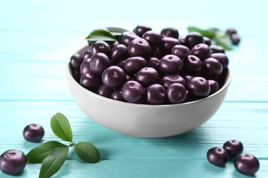 Tasty acai berries in bowl on light blue wooden table, closeup