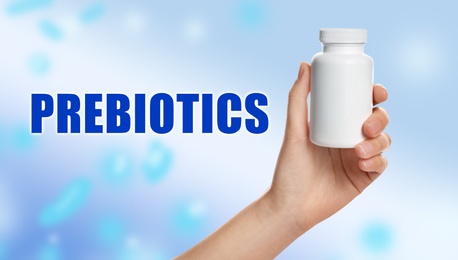 Image of Woman holding bottle of pills on light blue background, closeup. Prebiotic supplements