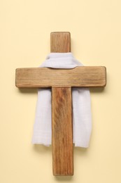 Wooden cross and white cloth on beige background, top view. Easter attributes