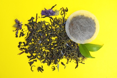 Tea bag with scattered dry leaves on color background, top view