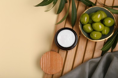 Photo of Jar of natural cream, olives and leaves on beige background, flat lay. Space for text