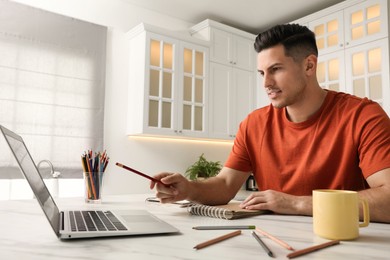 Photo of Man drawing in notebook at online lesson indoors. Distance learning
