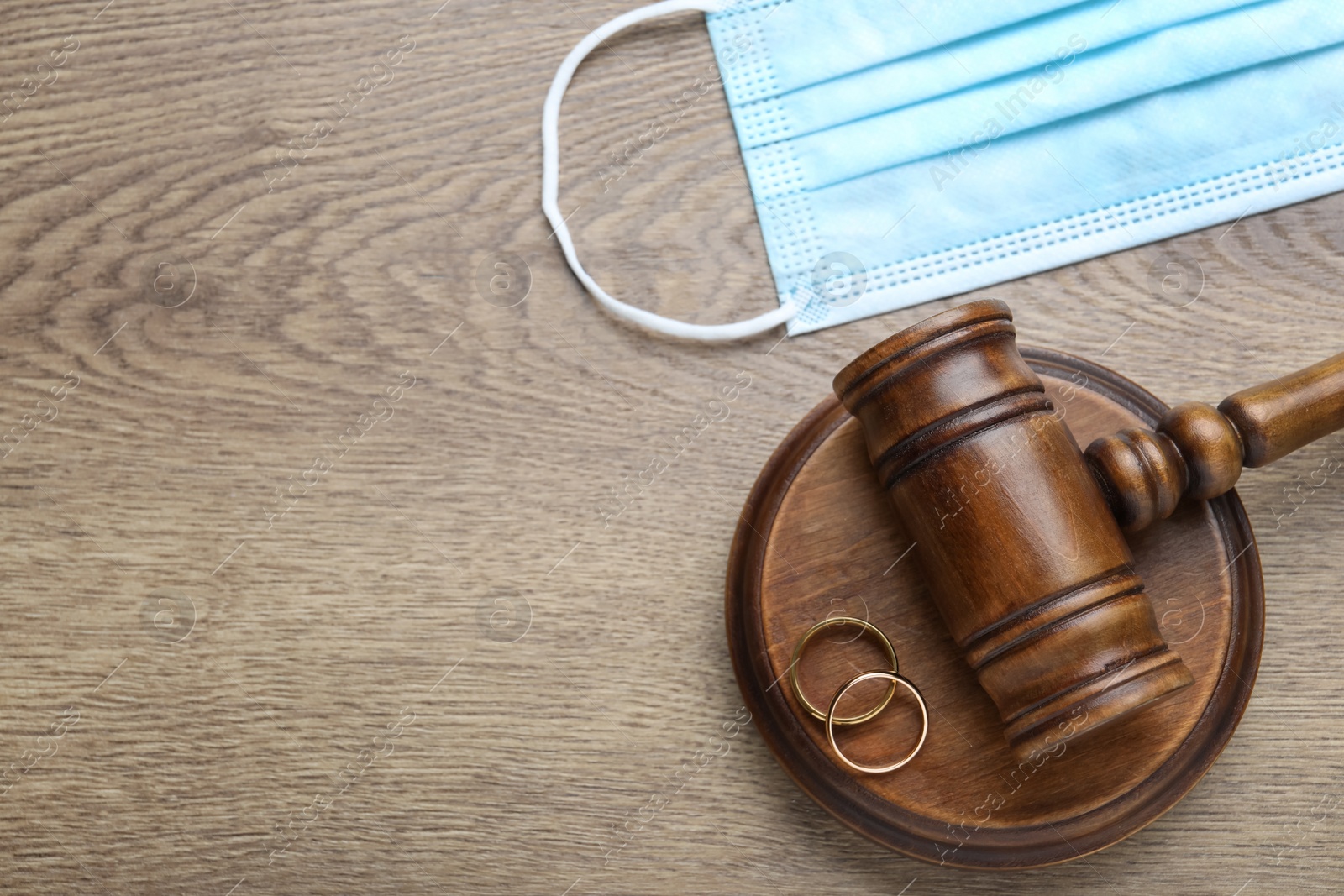 Photo of Gavel, protective mask and wedding rings on wooden table, flat lay with space for text. Divorce during coronavirus quarantine