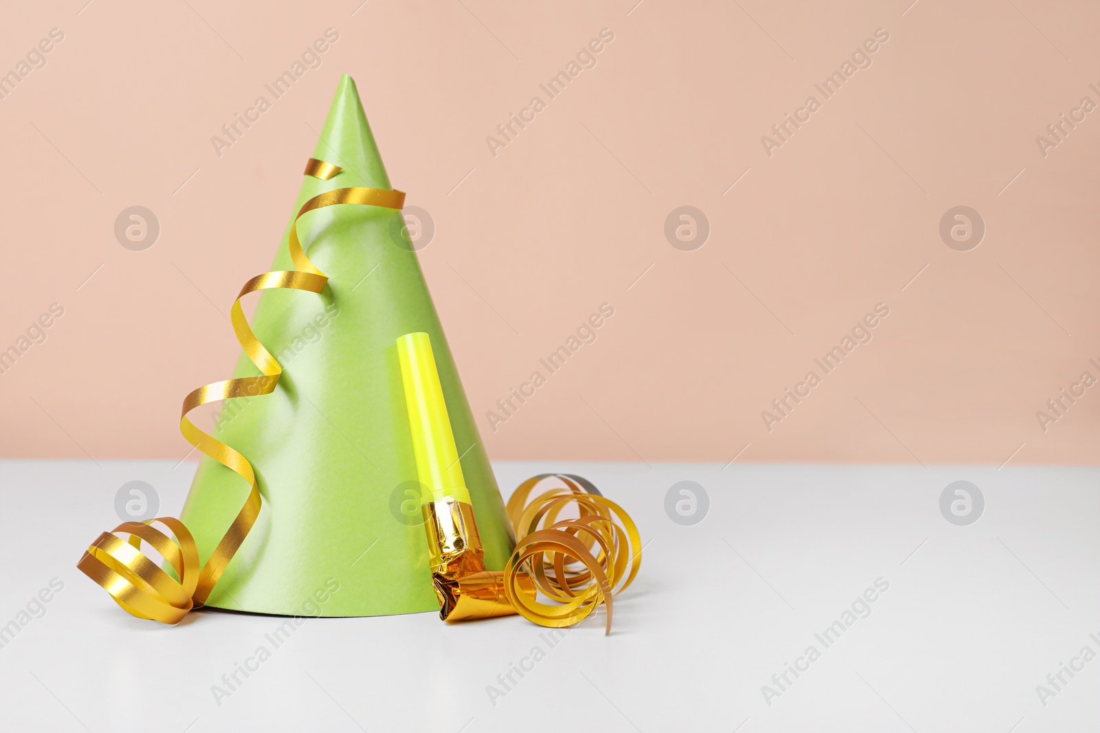 Photo of Colorful party hat, streamers and blower on white table, space for text. Birthday celebration