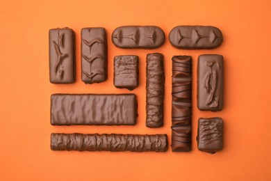 Photo of Different tasty chocolate bars on orange background, flat lay