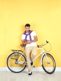 Photo of Handsome young hipster man with bicycle near yellow wall