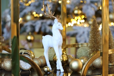 White deer figure, baubles and other Christmas decor on table against blurred background, closeup