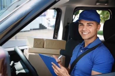 Photo of Young courier with parcels and clipboard in delivery car