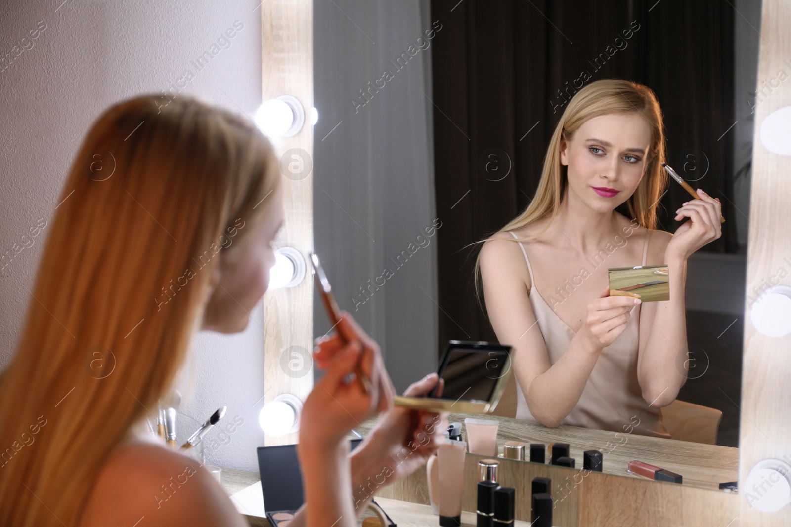 Photo of Beautiful woman applying makeup near mirror in room