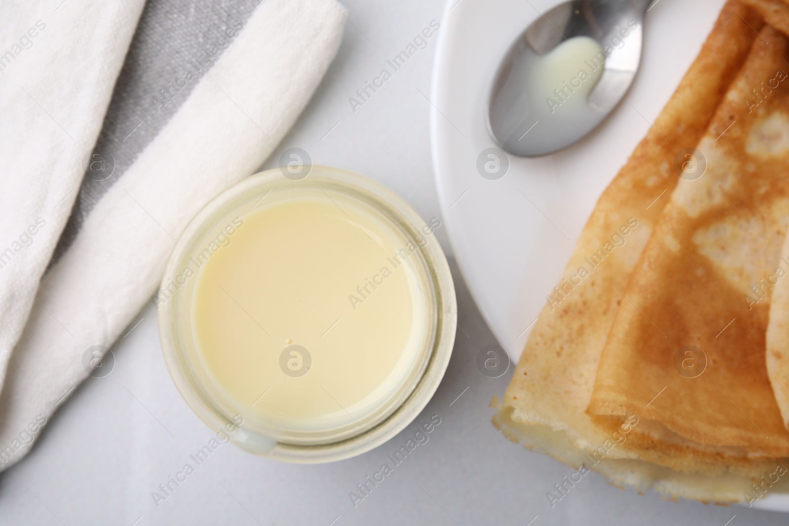 Tasty condensed milk in jar and crepes on white table, flat lay Photo of Tasty condensed milk in jar and crepes on white table, flat lay