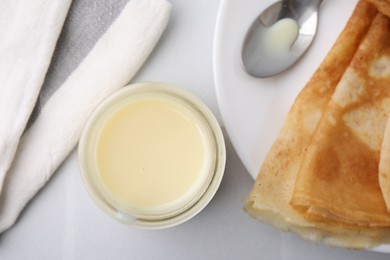 Photo of Tasty condensed milk in jar and crepes on white table, flat lay