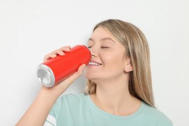 Photo of Beautiful woman drinking from red beverage can on light background