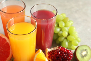 Three glasses of different juices and fresh fruits on table