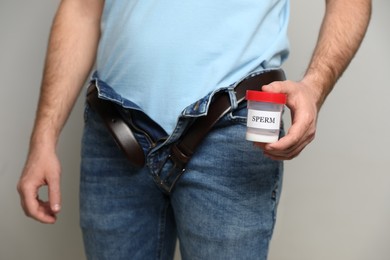 Photo of Donor with unzipped pants holding container of sperm on beige background, closeup