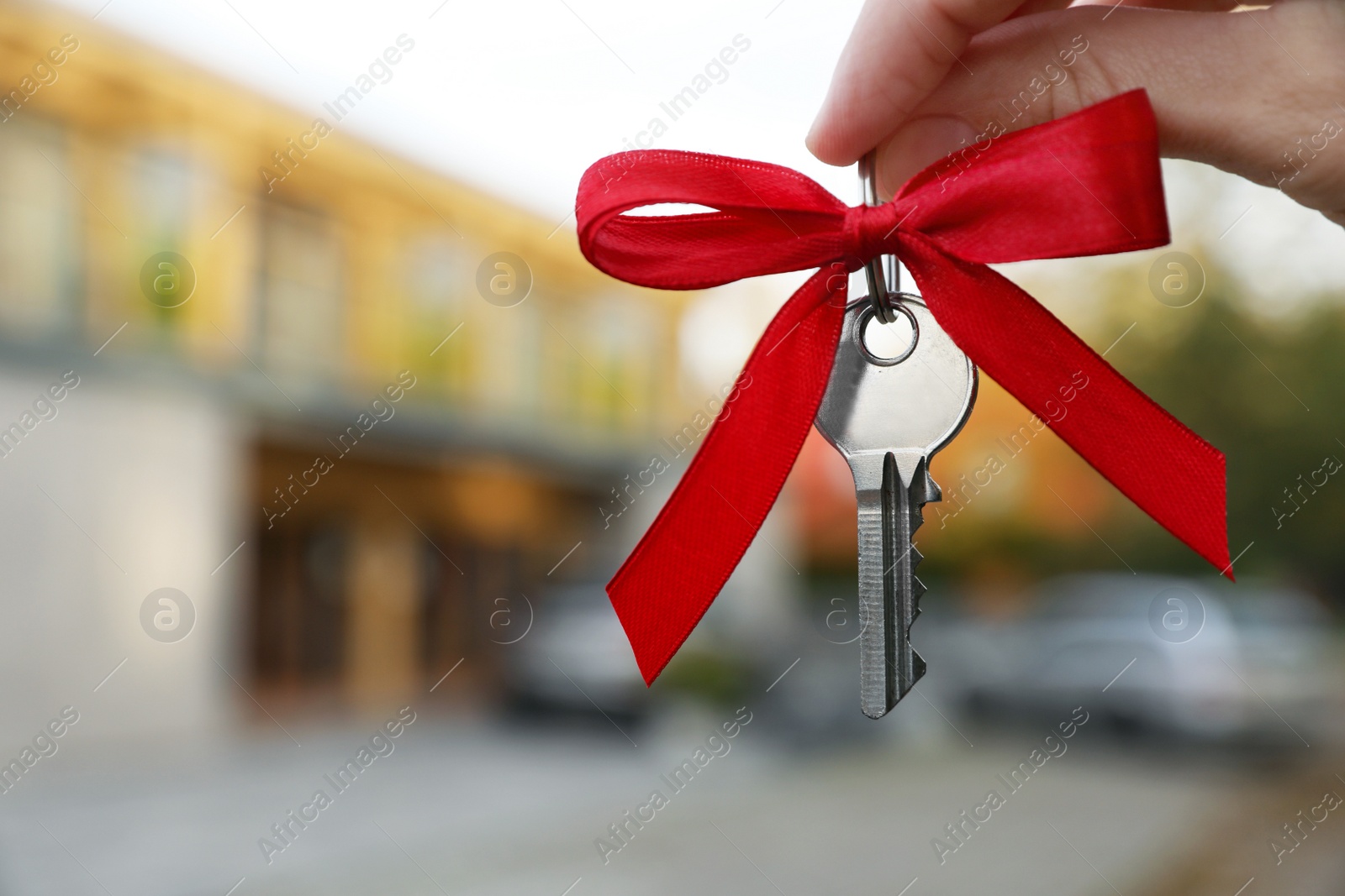 Photo of Woman holding key with bow near house outdoors, closeup. Space for text