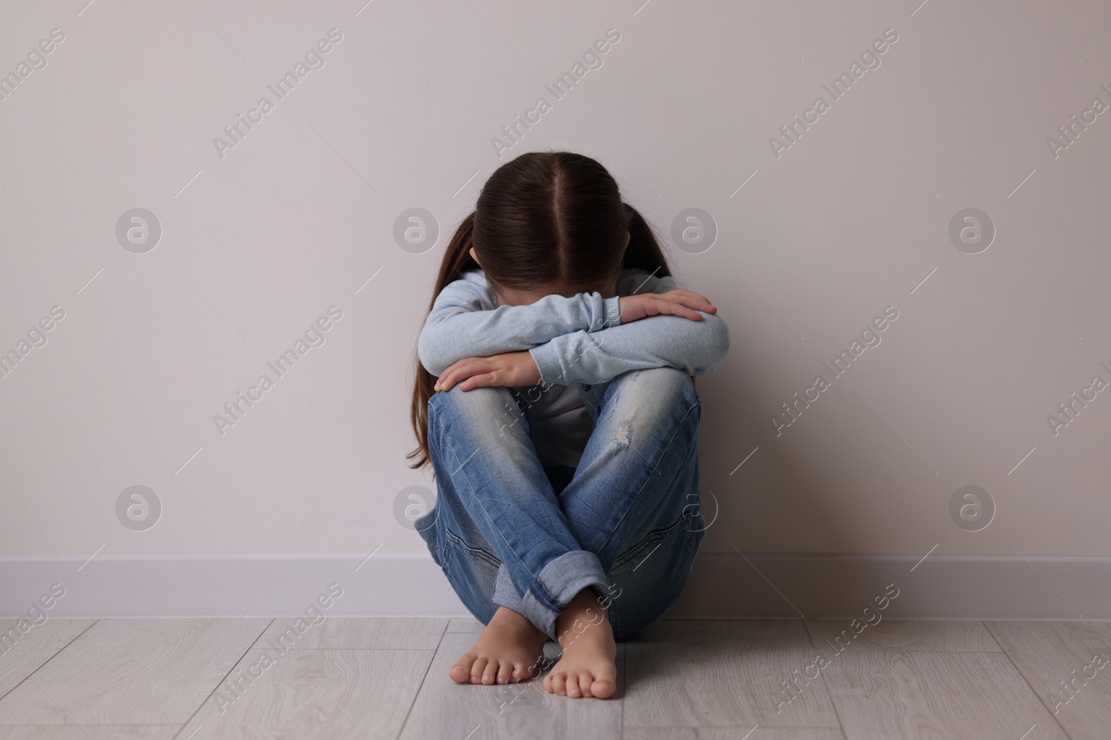 Photo of Child abuse. Upset little girl sitting on floor near light wall indoors