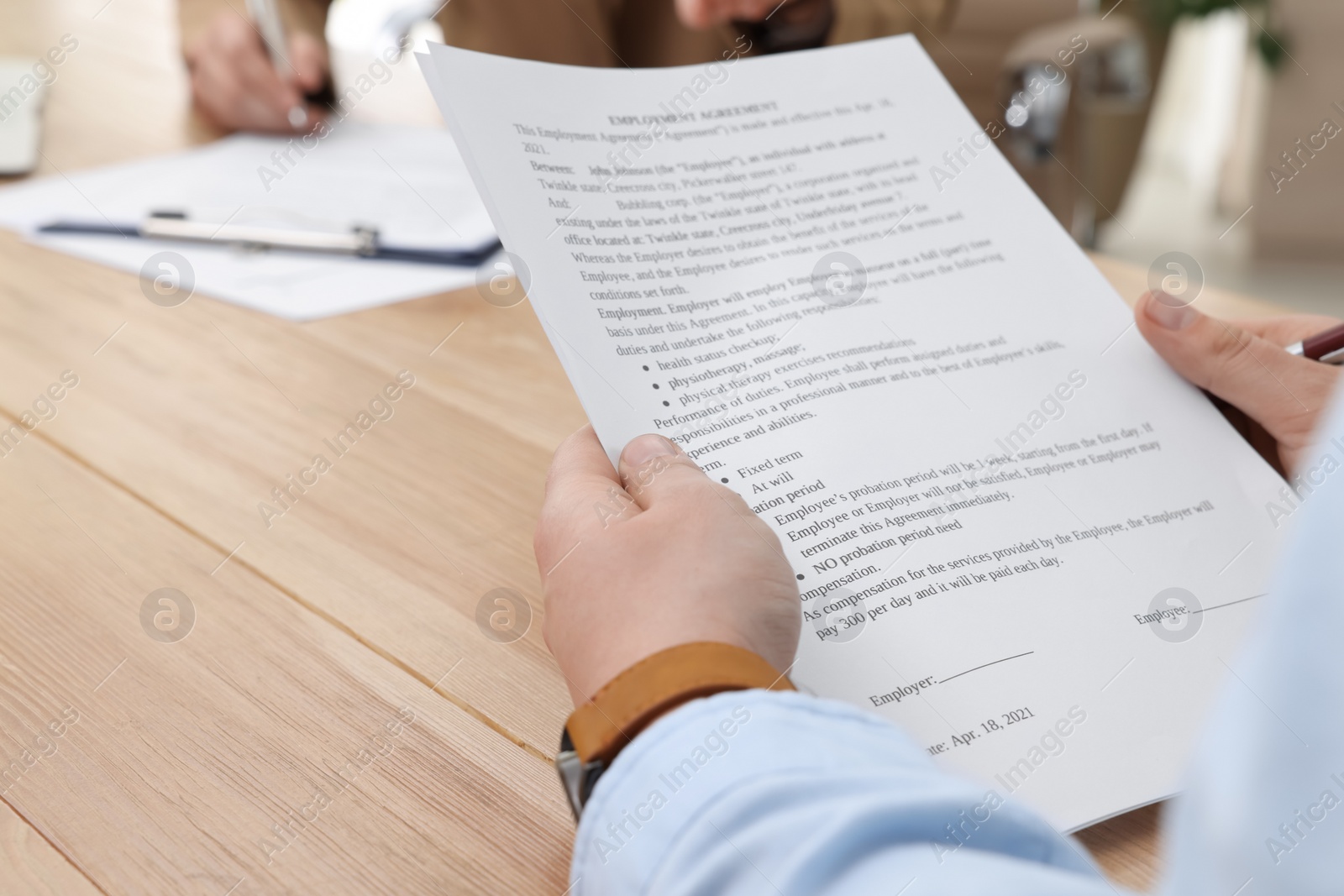 Photo of Man reading employment agreement at table in office, closeup. Signing contract