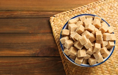 Photo of Brown sugar cubes in glass bowl on wooden table, top view. Space for text