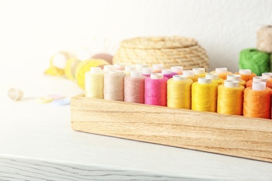 Photo of Wooden box with color sewing threads on table