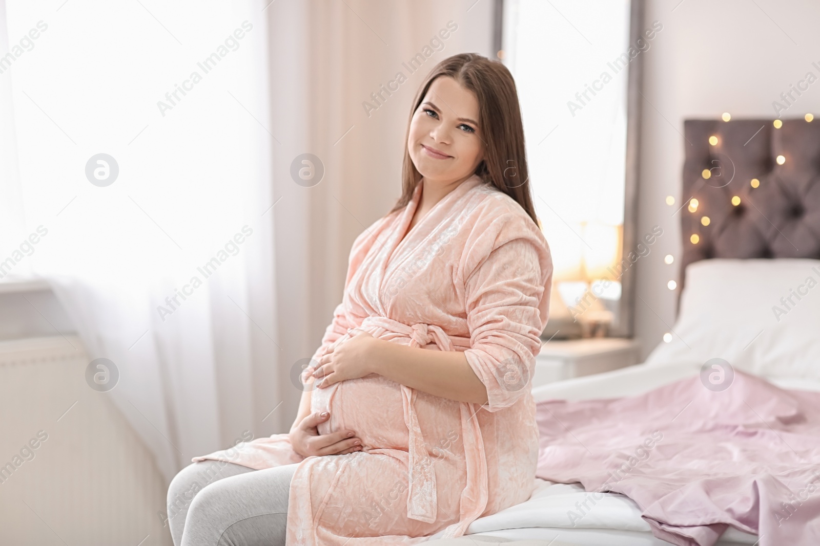 Photo of Beautiful pregnant woman sitting on bed at home