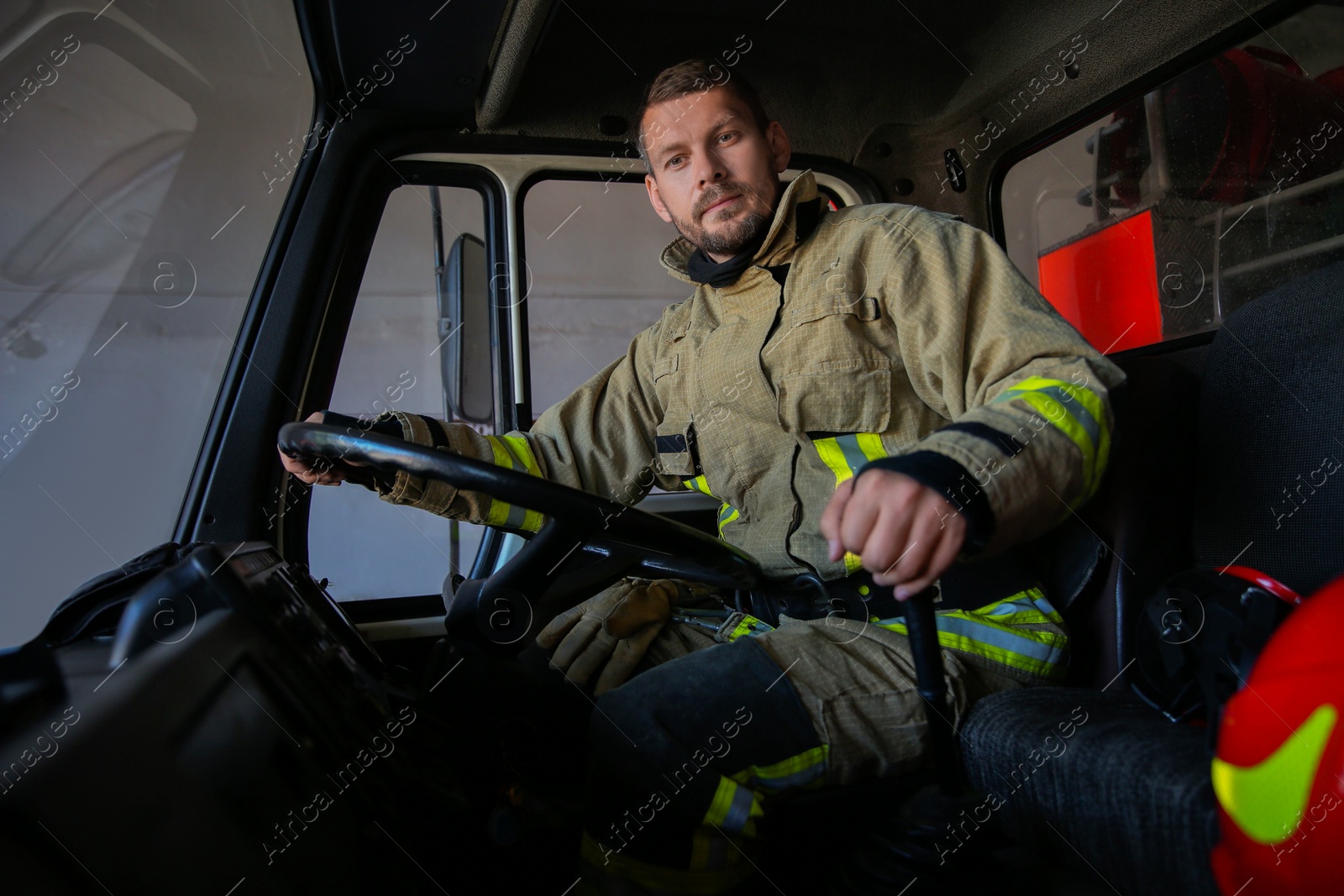 Photo of Firefighter in uniform driving modern fire truck